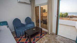 A room with a bed, two chairs, a small table, an air conditioning unit, a sliding glass door, and a view of the sea. - Lilly Rooms And Studios (Hurghada)