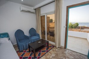 Una stanza con un letto, due poltrone, un tavolino, un condizionatore d'aria, una porta scorrevole in vetro e vista sul mare.