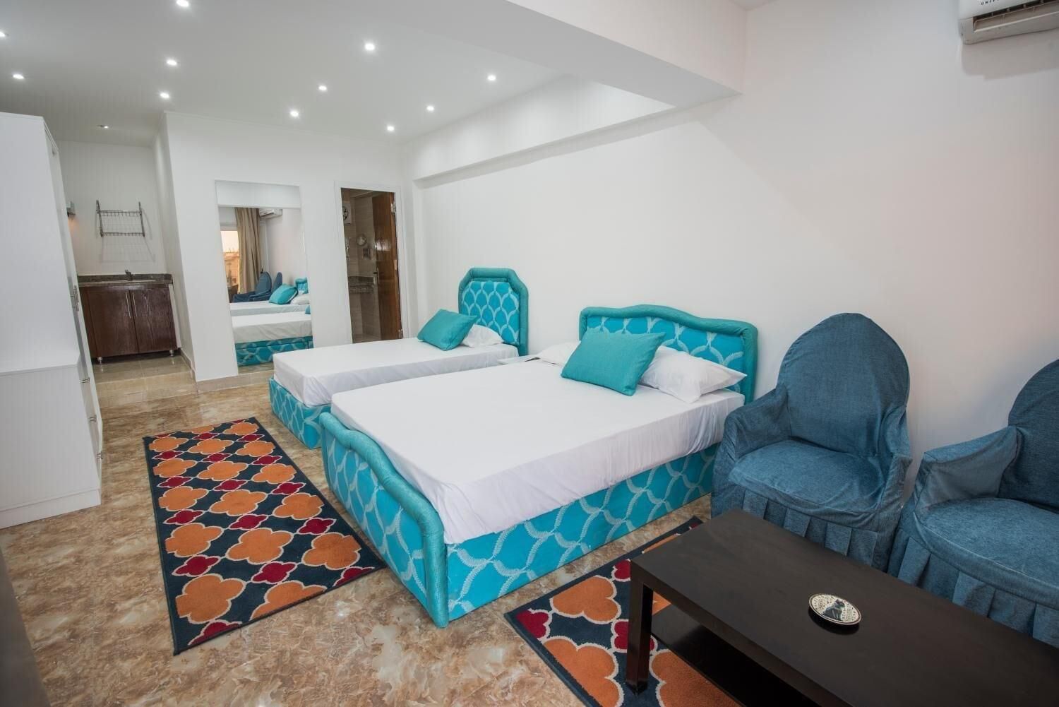 A hotel room with two beds, a small table, a chair, and a bathroom visible in the background.