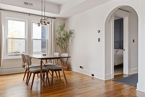A dining area with a wooden table and chairs, a hanging light fixture, and a view through a window with a brick wall. - Executive Suite/ Walkable/ Free Parking/ Office #5 (Lakewood)