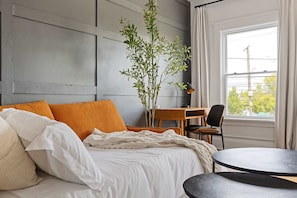 A neatly made bed with white and orange bedding, a small round table, and a desk with a chair. A potted plant is placed on the desk. - Executive Suite/ Walkable/ Free Parking/ Office #5 (Lakewood)