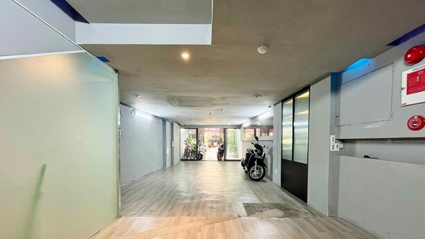 Un pasillo con piso de madera, una motocicleta estacionada a la derecha y un detector de incendios en la pared.