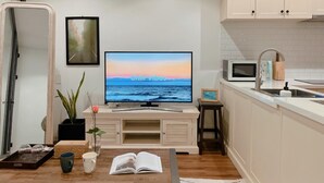 Una cocina moderna con televisión de pantalla plana, microondas, pileta y un pequeño comedor.