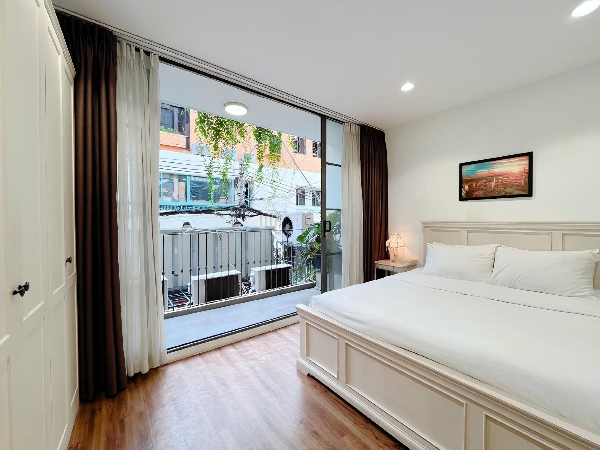 A hotel room with a large sliding glass door, a bed with white linens, a small bedside table with a lamp, and a painting on the wall.