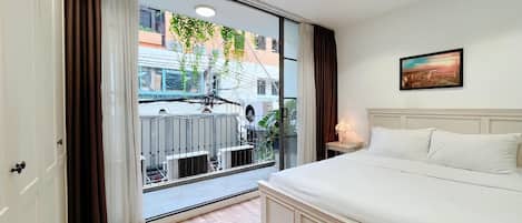 Une chambre d’hôtel dotée d’une grande porte-fenêtre coulissante, d’un lit avec du linge de lit blanc, d’une petite table de chevet avec une lampe et d’un tableau au mur.