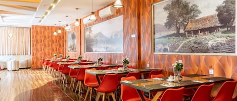 A restaurant with multiple tables, red chairs, and large framed pictures on the walls.