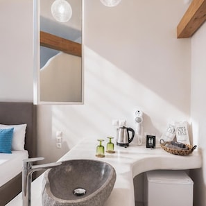 Un baño moderno con un lavabo de piedra, un espejo, un hervidor de agua y un secador de pelo en la encimera.