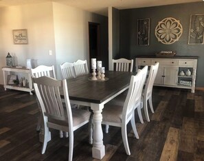 A dining area with a dark wooden table surrounded by white chairs, a white cabinet with decorative items, and a dark wall with floral artwork.