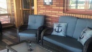 Ein überdachter Patio-Bereich mit Korbmöbeln, einer Wanddekoration aus Metall und Blick durch ein Fenster.