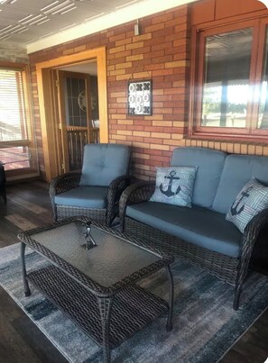 Un patio cubierto con muebles de mimbre, un adorno metálico en la pared y vistas a través de una ventana.