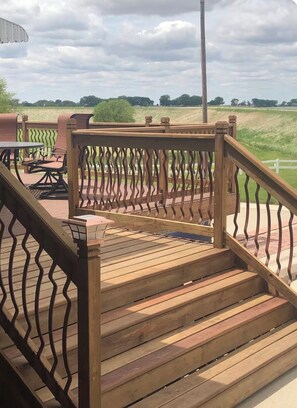 Una terraza de madera con barandilla, una mesa con sillas y vistas a un campo cubierto de césped.