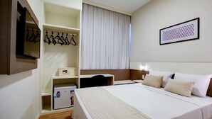 A hotel room with a bed, a desk, a wardrobe, and a mirror.