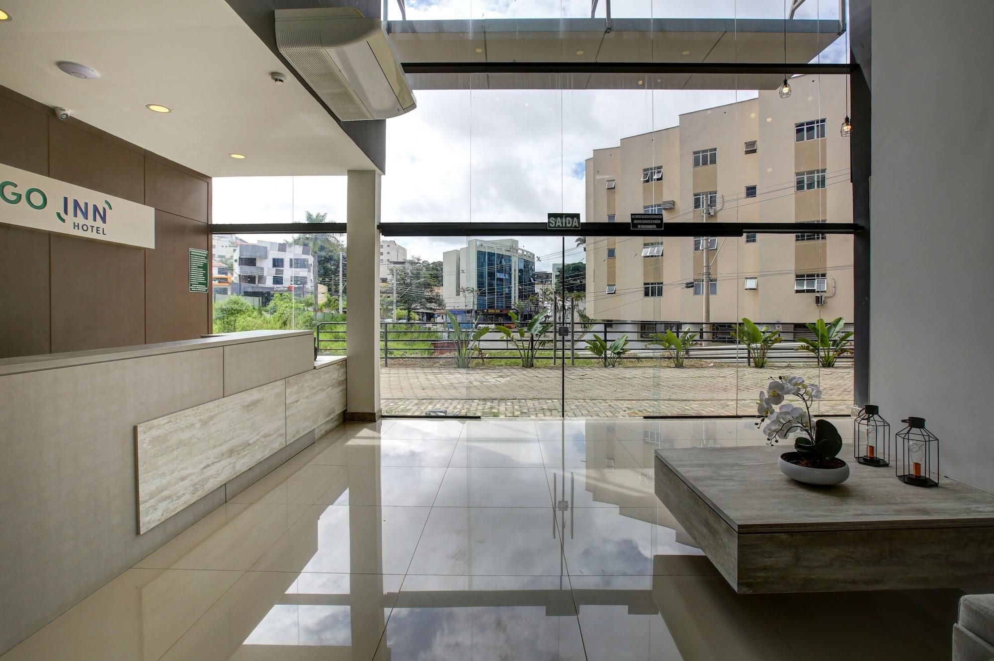A modern hotel reception area with a glass wall, a reception desk, and a view of the cityscape.