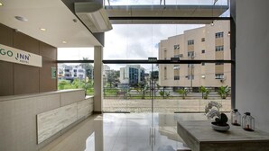 A modern hotel reception area with a glass wall, a reception desk, and a view of the cityscape.