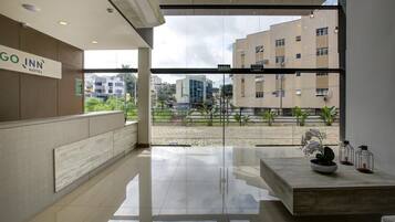 A modern hotel reception area with a glass wall, a reception desk, and a view of the cityscape.