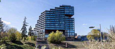 A modern building with multiple floors, a river in the foreground, and a clear sky.