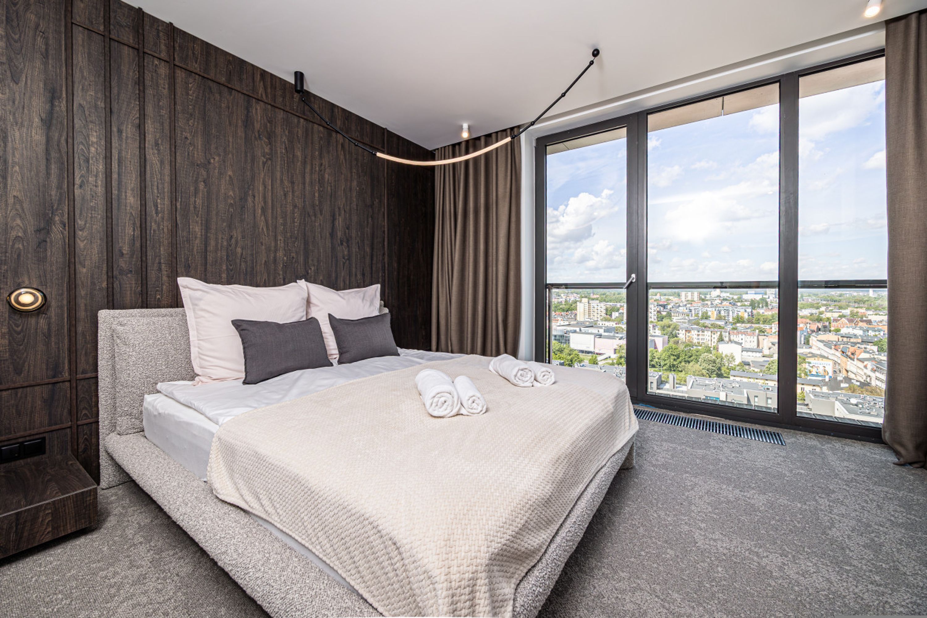 A modern hotel room with a large bed, a city view, and a wooden accent wall.