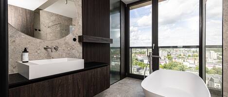 A modern bathroom with a freestanding bathtub, a large mirror, and a view of a cityscape through large windows.