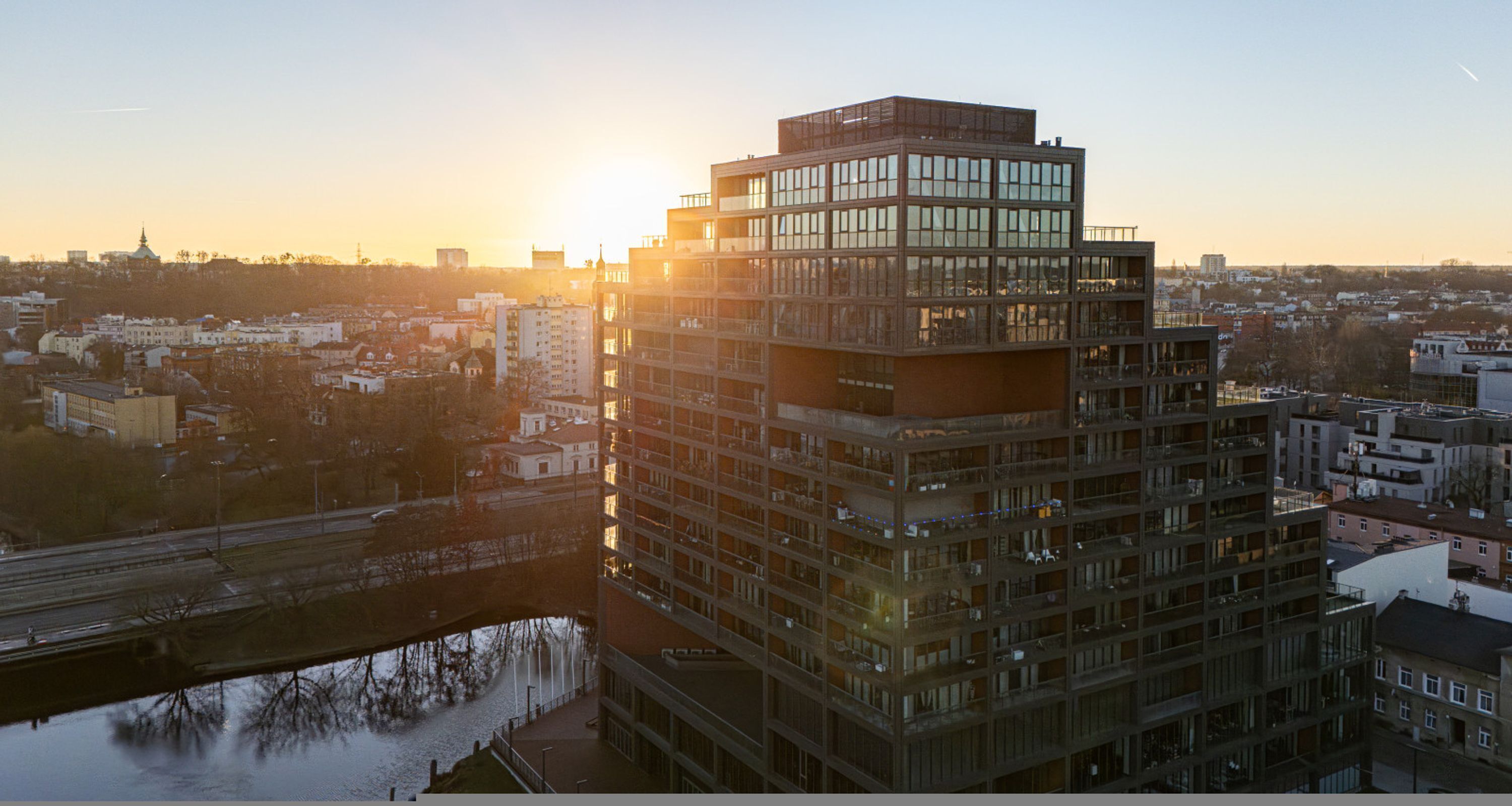 Un edificio de varios pisos con un diseño arquitectónico moderno, que destaca por un amplio frente de vidrio y una terraza en la azotea.