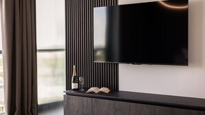 Ein modernes Wohnzimmer mit einem Flachbildfernseher an einer dunklen Holzkonsol, einer Weinflasche und einem offenen Buch.