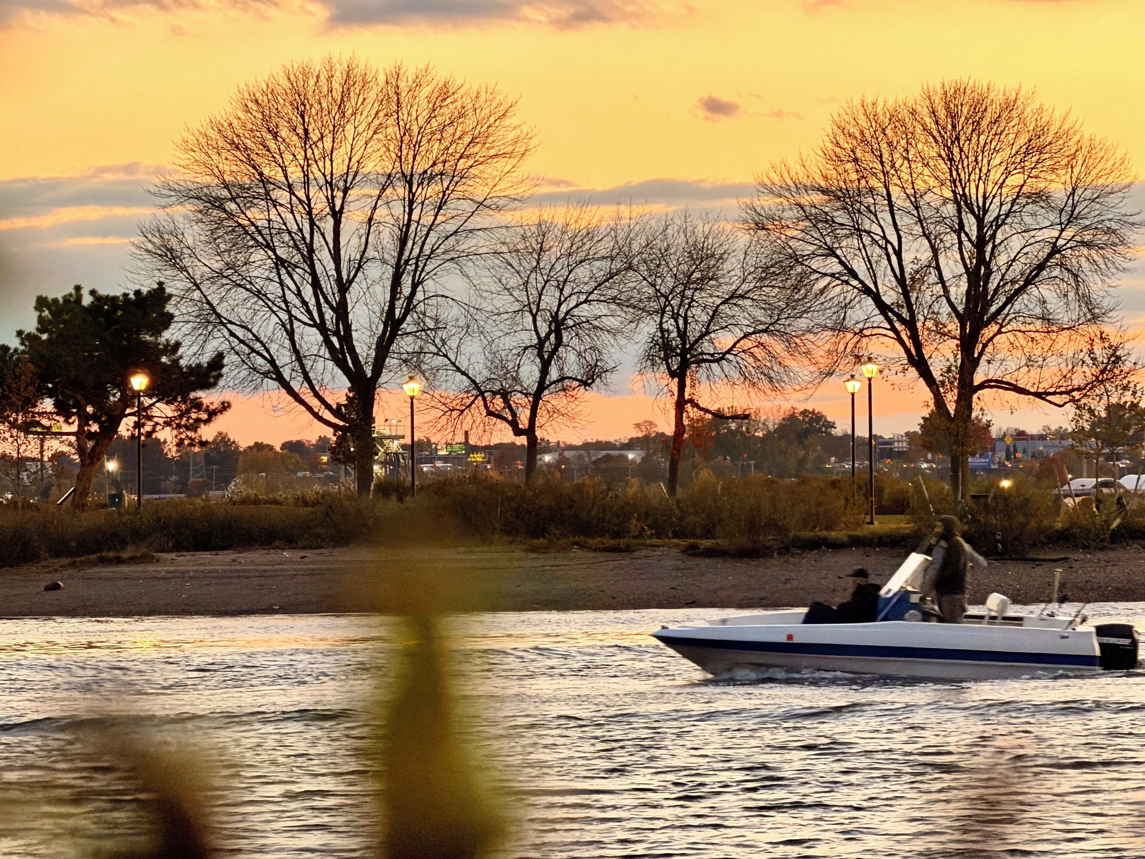 A boat on a body of water with trees and street lamps in the background.