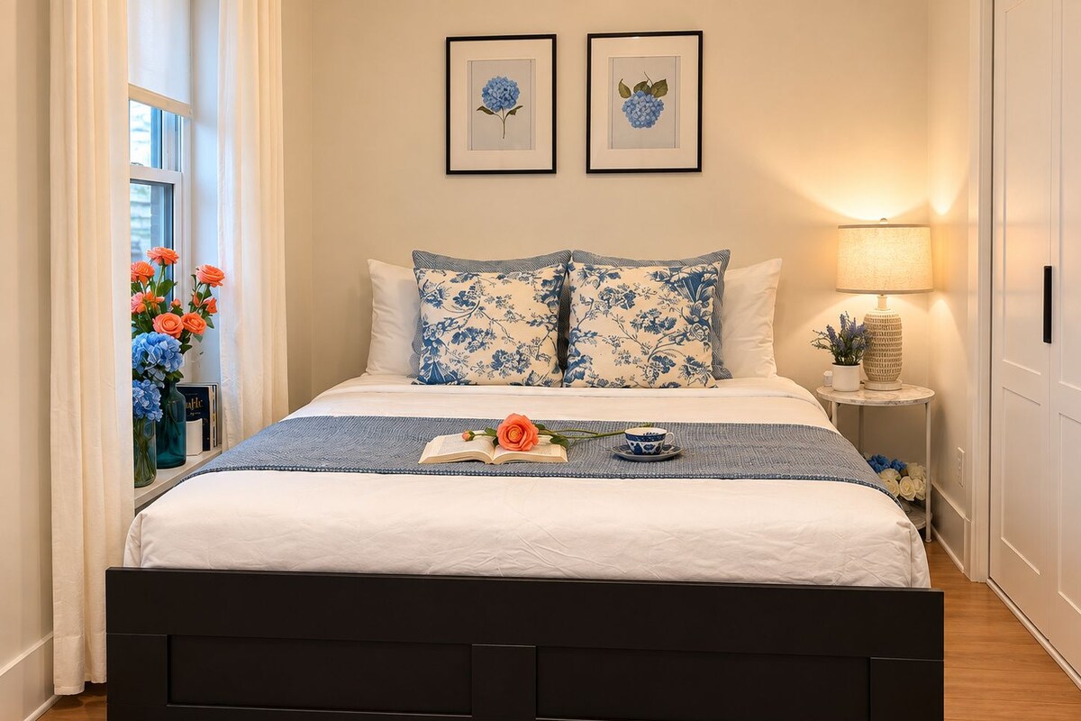A neatly made bed with a blue and white floral duvet, a black headboard, and a bedside table with a lamp.