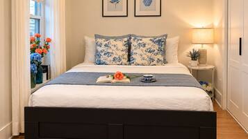 Una cama bien tendida con cubrecama azul y blanco estampado floral, cabecera negra y mesita de noche con lámpara.