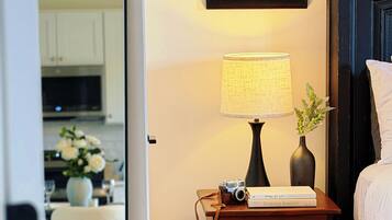 A bedroom with a bed, bedside table with a lamp, a framed picture, and a mirror reflecting a dining area.