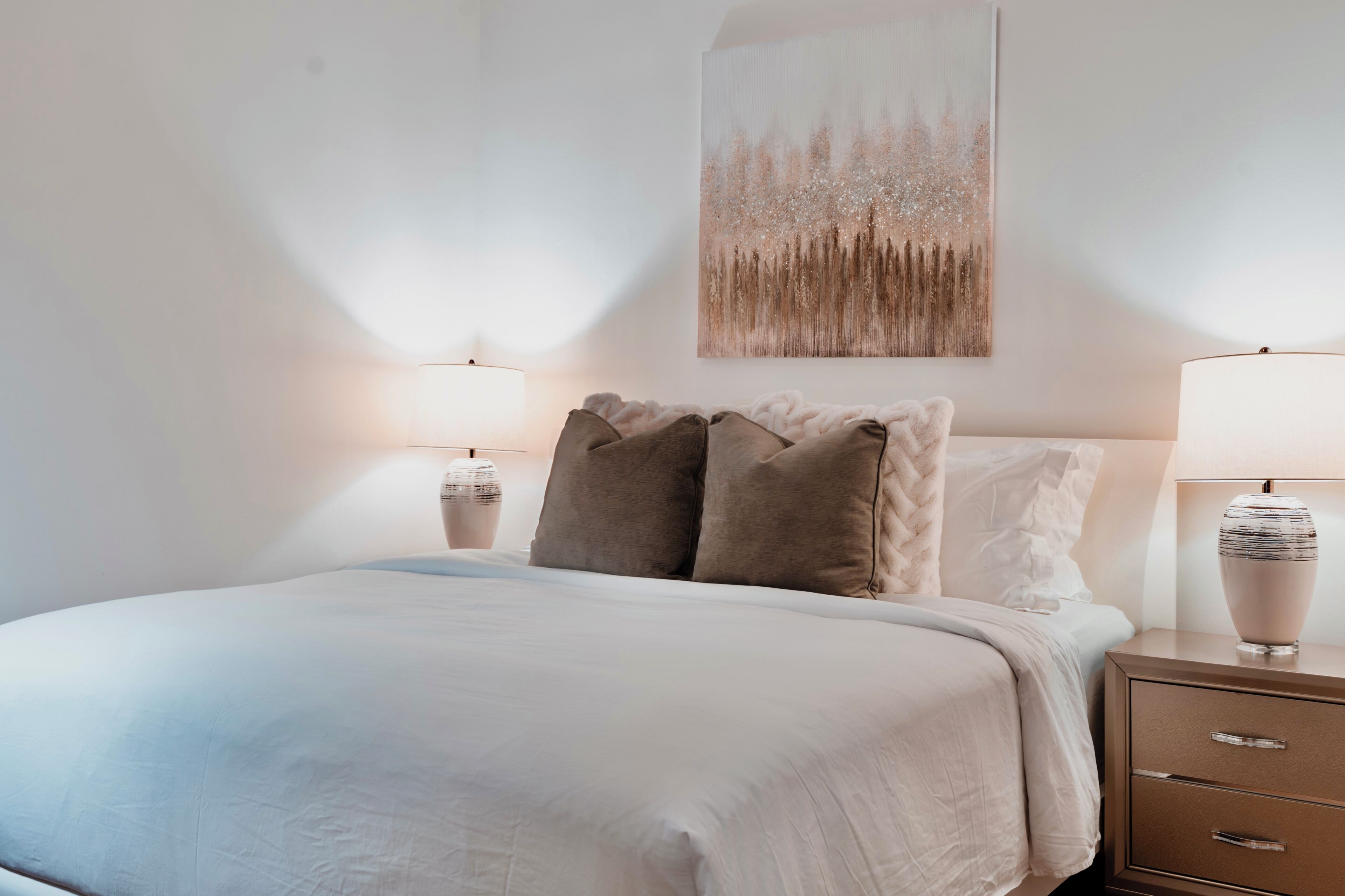 Ein ordentlich bezogenes Bett mit weißer Decke und zwei Kissen, begleitet von Nachttischen mit Lampen.