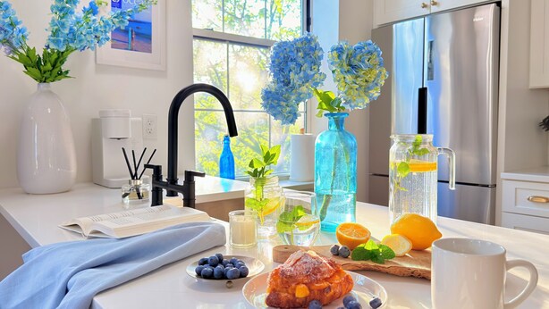 A kitchen with a white countertop, a sink, a refrigerator, and a window with blue flowers. - Fox Point Landing Residences (Providence)