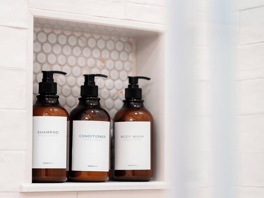 A bathroom shelf with three bottles of shampoo, conditioner, and body wash from the Margaux Collection.