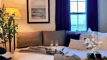 A hotel room with a bed, a bedside table with a lamp, a framed picture on the wall, and a view of the sea through the window.