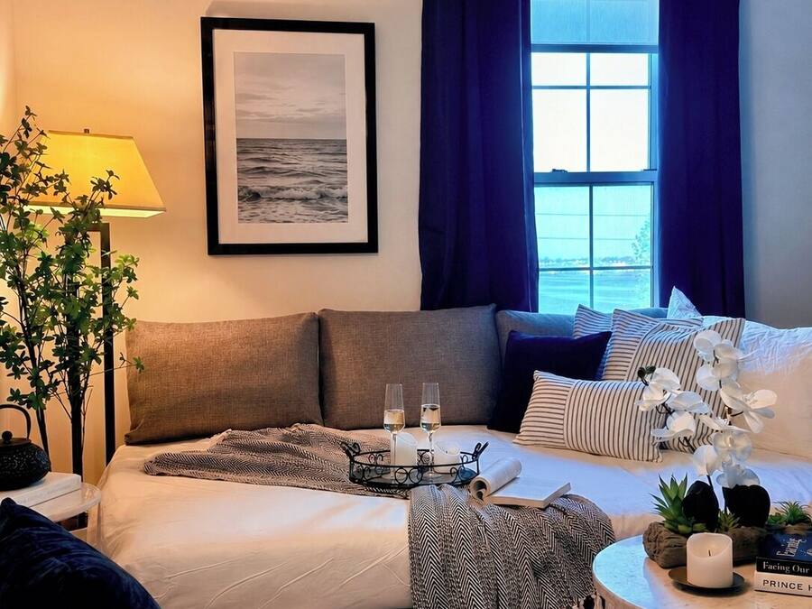A hotel room with a bed, a bedside table with a lamp, a framed picture on the wall, and a view of the sea through the window.