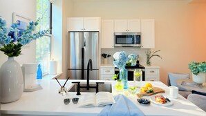 A modern kitchen with white cabinets, stainless steel appliances, and a dining area with a table set for two. - Fox Point Landing Residences (Providence)