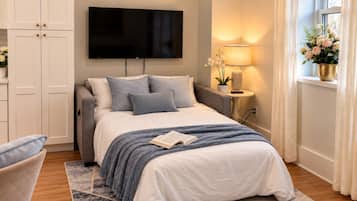 Een moderne slaapkamer met een bed, een televisie, een nachtkastje met lamp en een raam met gordijnen.