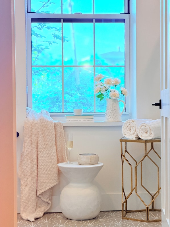 A bathroom with a window, a vase with flowers, a bowl, and towels on a table. - Fox Point Landing Residences (Providence)