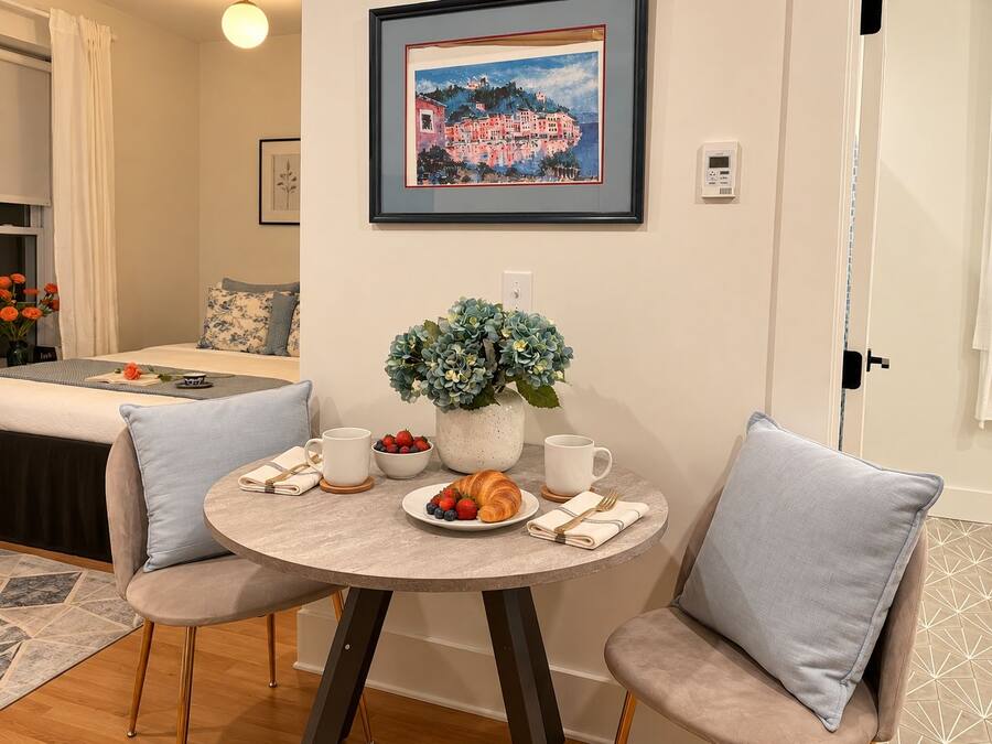 A dining area with a round table, two chairs, a vase of flowers, a plate of fruit, and a croissant.