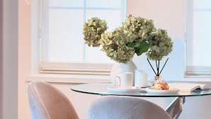 A dining area with two chairs, a table, a vase with flowers, a lamp, and a window with blinds. - Fox Point Landing Residences (Providence)