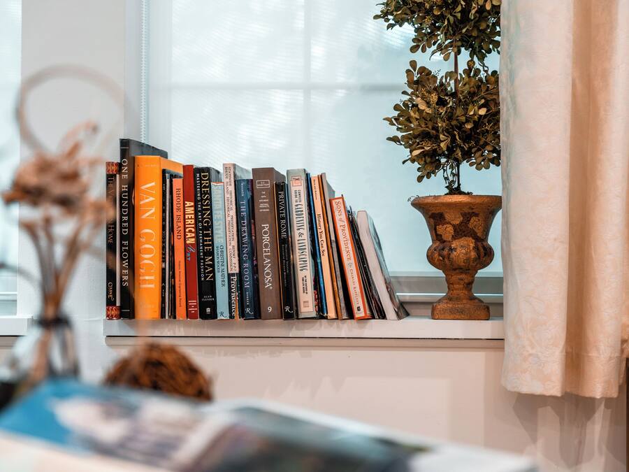 A bookshelf with a variety of books, a potted plant, and a window with curtains.