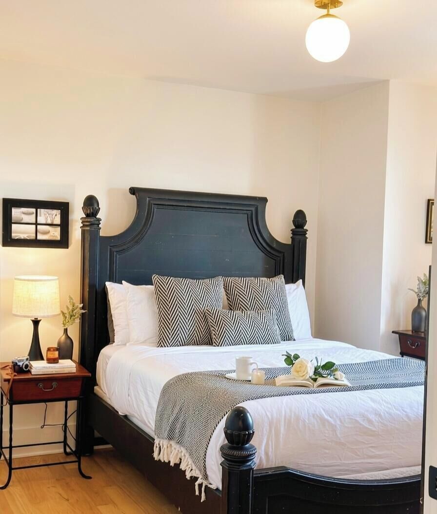 A neatly made bed with a dark headboard, a bedside table with a lamp, and a framed picture on the wall.