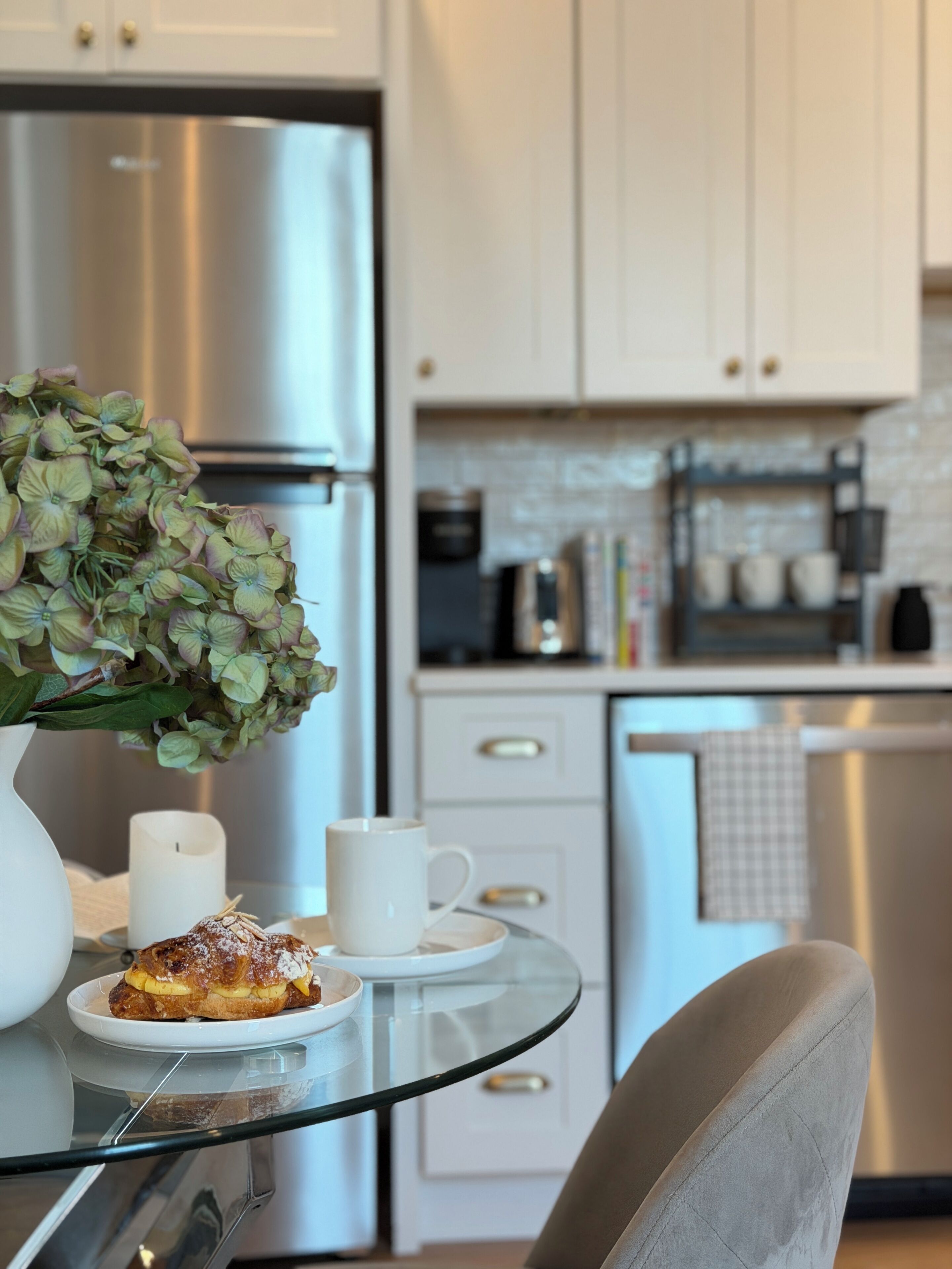 Une cuisine moderne avec des appareils en acier inoxydable, une table en verre et une chaise blanche.