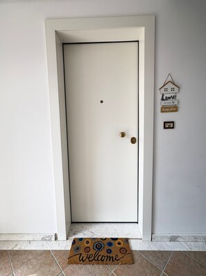 Uma porta branca com puxador de latão, um tapete de boas-vindas e um enfeite de parede com uma casa e texto.