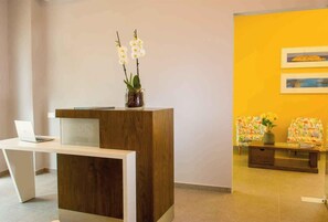 Un comptoir d’accueil avec un ordinateur portable, un espace d’accueil en bois et un mur jaune orné d’œuvres d’art encadrées.