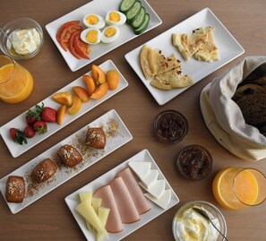 A variety of food items arranged on a table, including sliced fruits, cheeses, and bread. - Elounda Colour (Agios Nikolaos)
