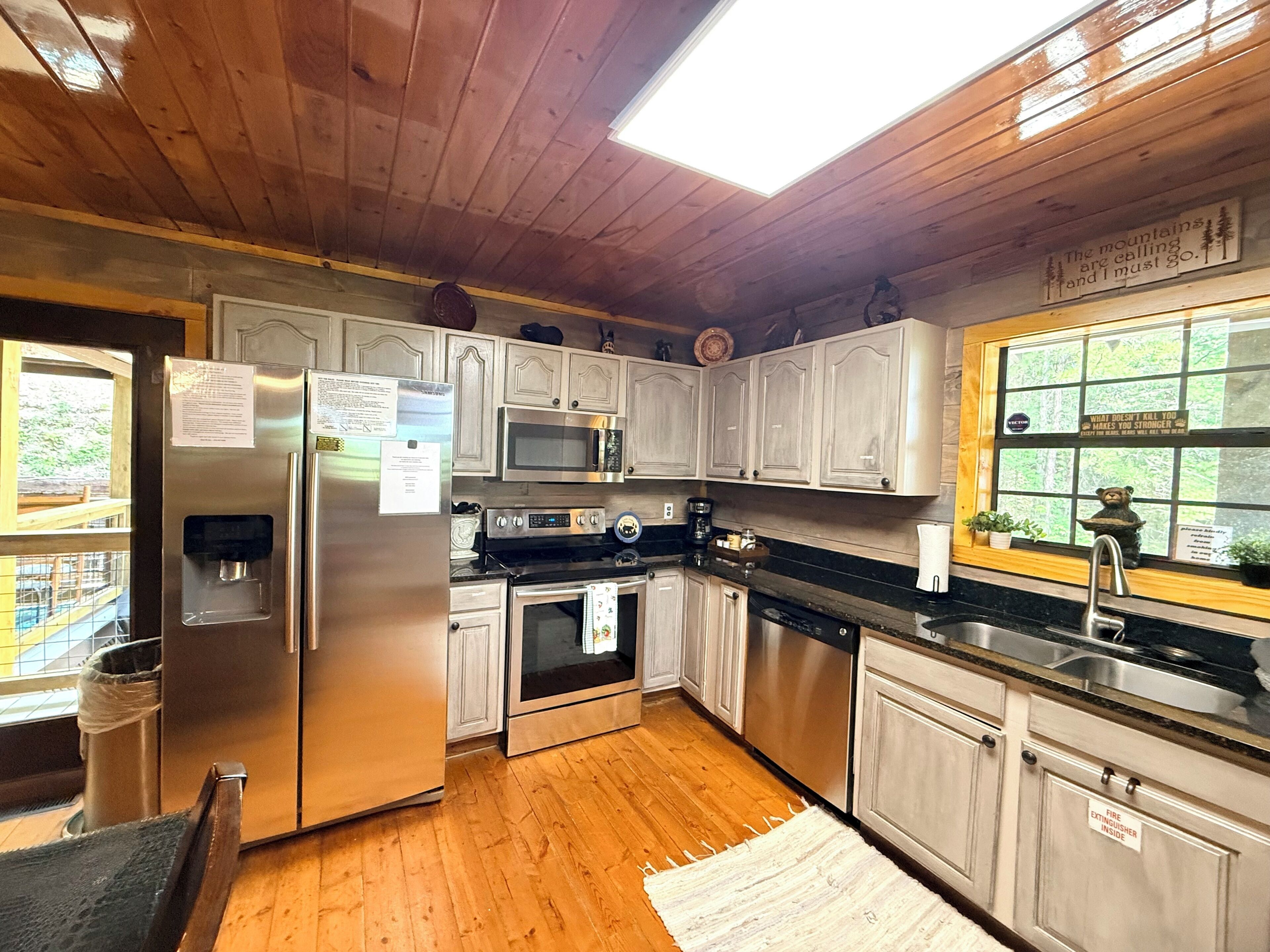 A kitchen with wooden cabinets, stainless steel appliances, a water dispenser, and a window with a view of trees.