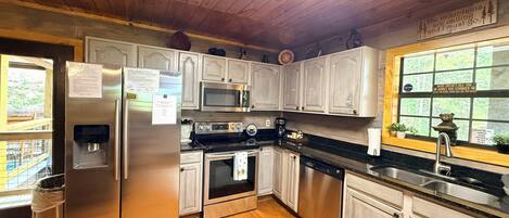 A kitchen with wooden cabinets, stainless steel appliances, a water dispenser, and a window with a view of trees.