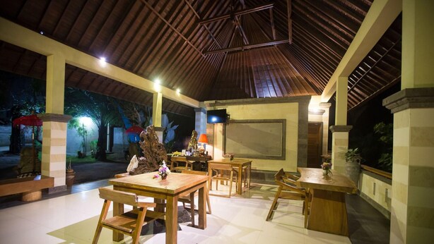 A spacious indoor area with wooden tables and chairs, a large screen, and a view of the outdoors. - Asri Sari Resort Ubud (Ubud)