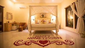 A honeymoon suite with a four-poster bed, a vanity with a mirror, and a decorative heart-shaped flower arrangement on the floor. - Asri Sari Resort Ubud (Ubud)