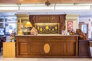 Una mesa de recepción con un letrero que dice 'JUNTRA Resort & Hotel' y varios objetos decorativos, incluyendo una estatua de Buda, una lámpara y una escultura de dragón.