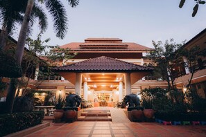 Entrada de hotel con tejado de baldosas, un corredor cubierto y una zona de recepción con una estatua.